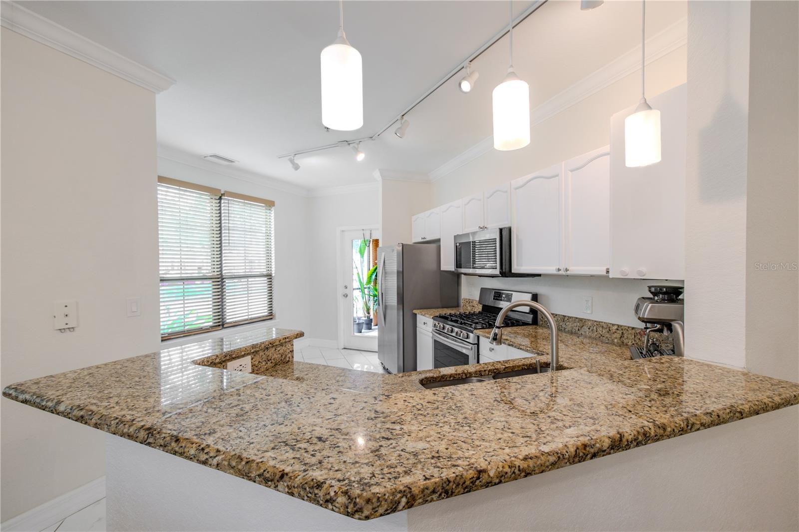 The kitchen’s generous granite peninsula, which serves as both a functional workspace and a natural gathering point. The expansive counter provides ample prep space and seating potential, while pendant lighting above adds soft, focused illumination.