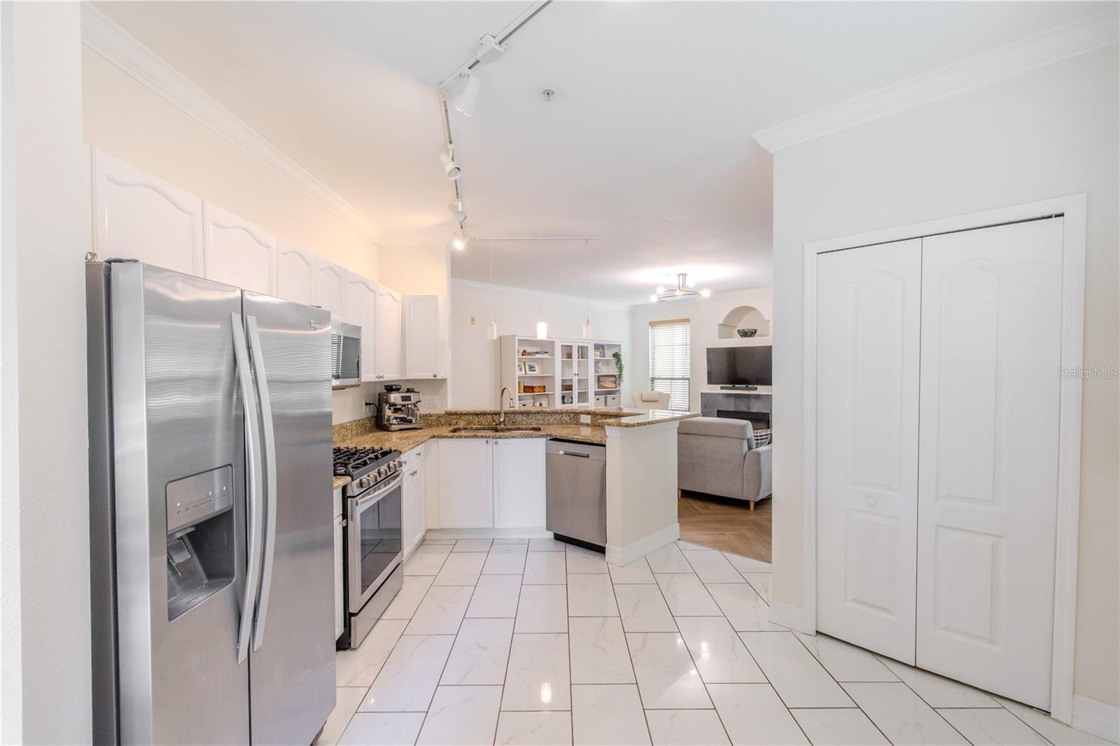 The tiled kitchen floor offers durability and easy maintenance, while track lighting and pendant fixtures provide layered illumination throughout and a closet a pantry, completing a kitchen that feels both practical and well-connected to the rest of the home.