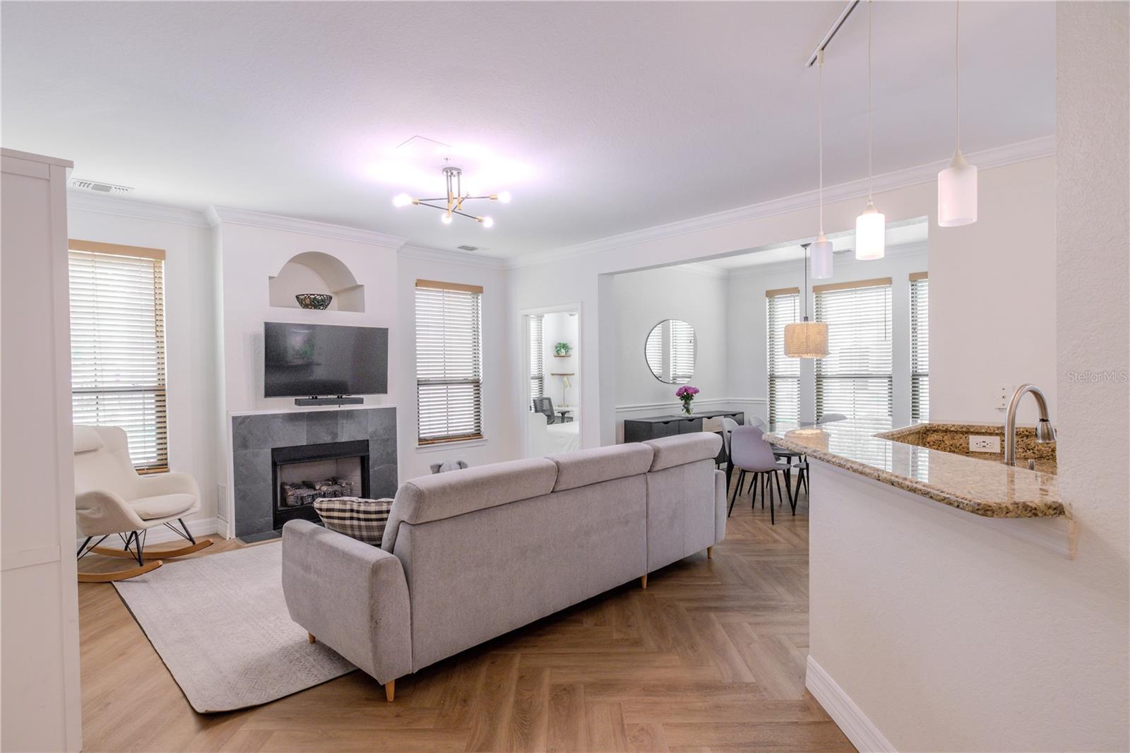 Spacious open-concept living area with chevron luxury vinyl plank flooring, a modern fireplace, and seamless flow into the dining space beyond.