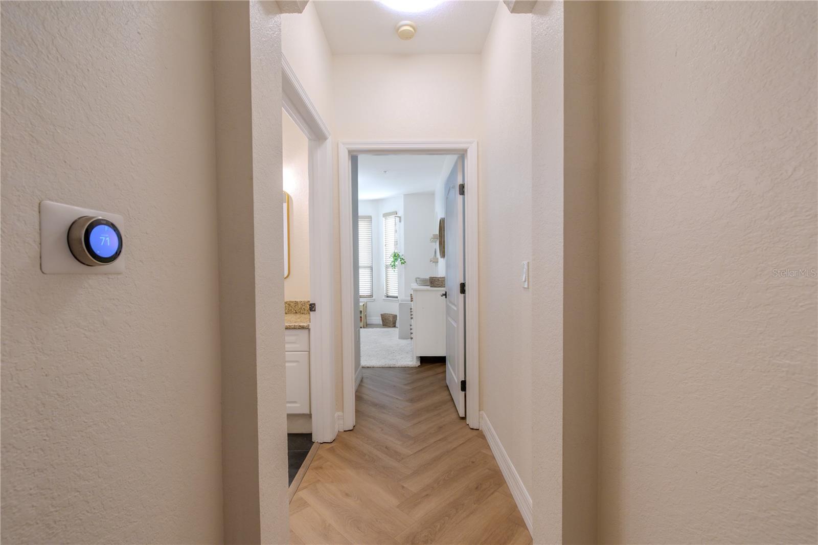 Light-filled hallway featuring chevron luxury vinyl plank flooring and a clean, cohesive flow leading to the private bedroom and bath.