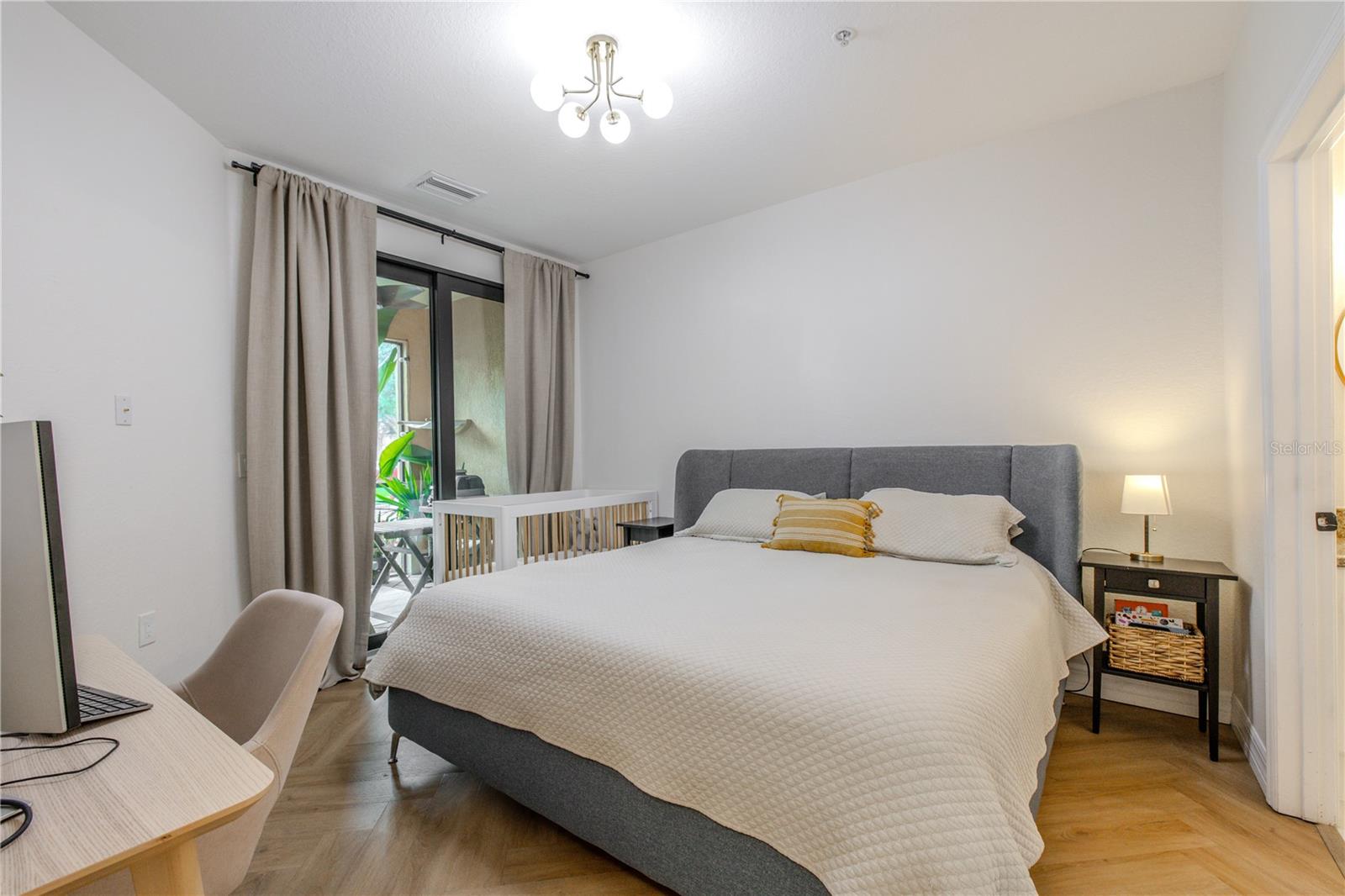 Serene primary bedroom  featuring chevron luxury vinyl plank flooring, a modern statement light fixture, soft natural light, and sliding glass doors opening to the covered patio.