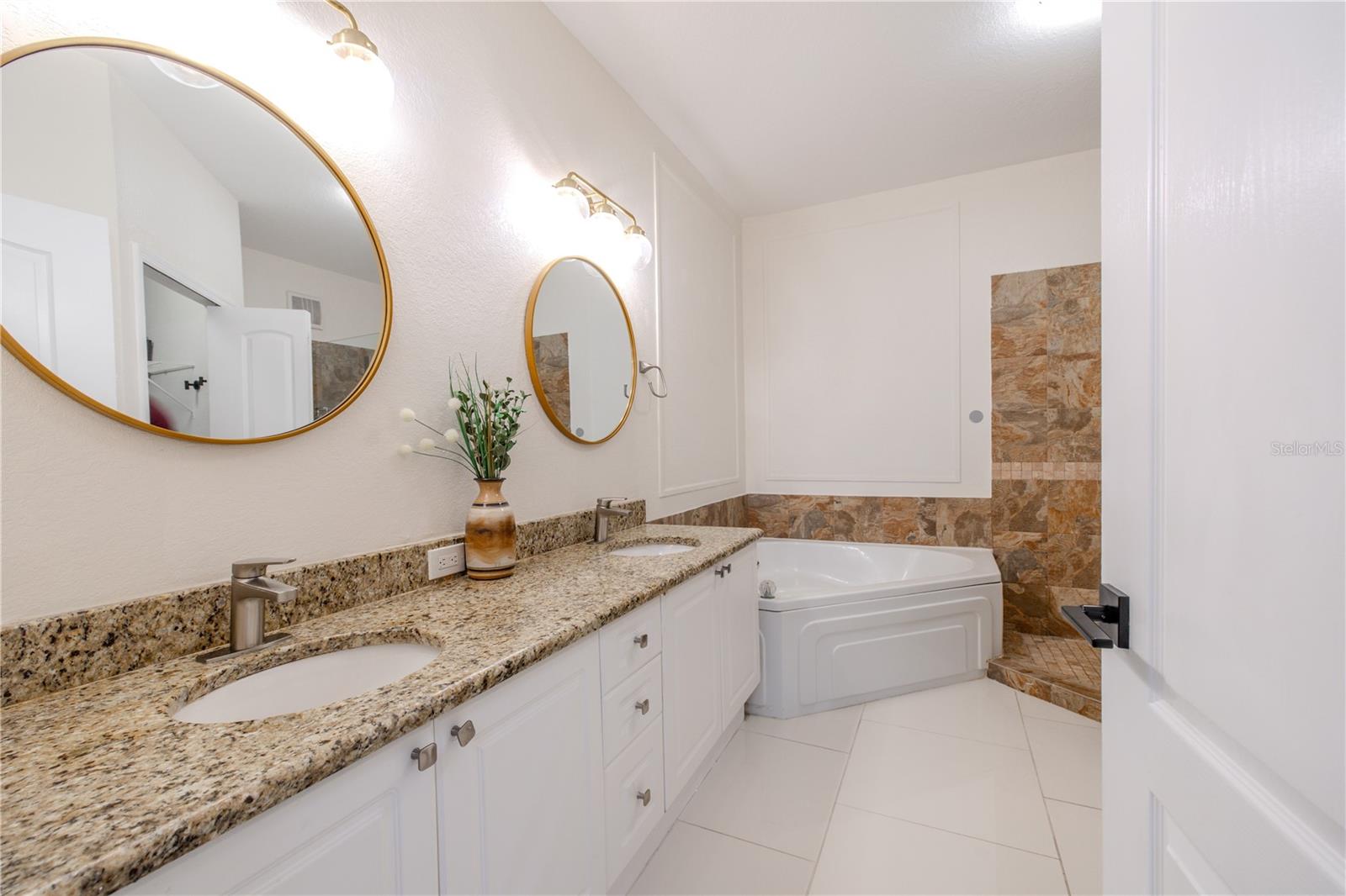 The spa-inspired primary bath includes a granite-topped vanity with undermount sink, crisp cabinetry, elegant lighting, a soaking tub, and a glass-enclosed walk-in shower w/natural stone tile, built-in niche, & multi-function shower system.