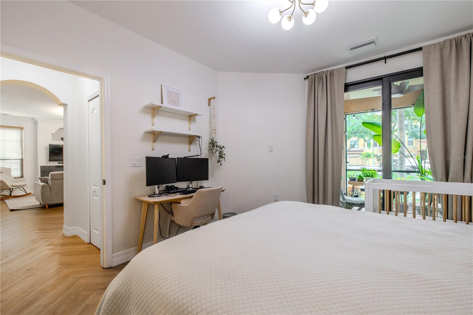 The primary bedroom features soft natural light, a modern statement light fixture, & sliding glass doors opening to the covered patio
