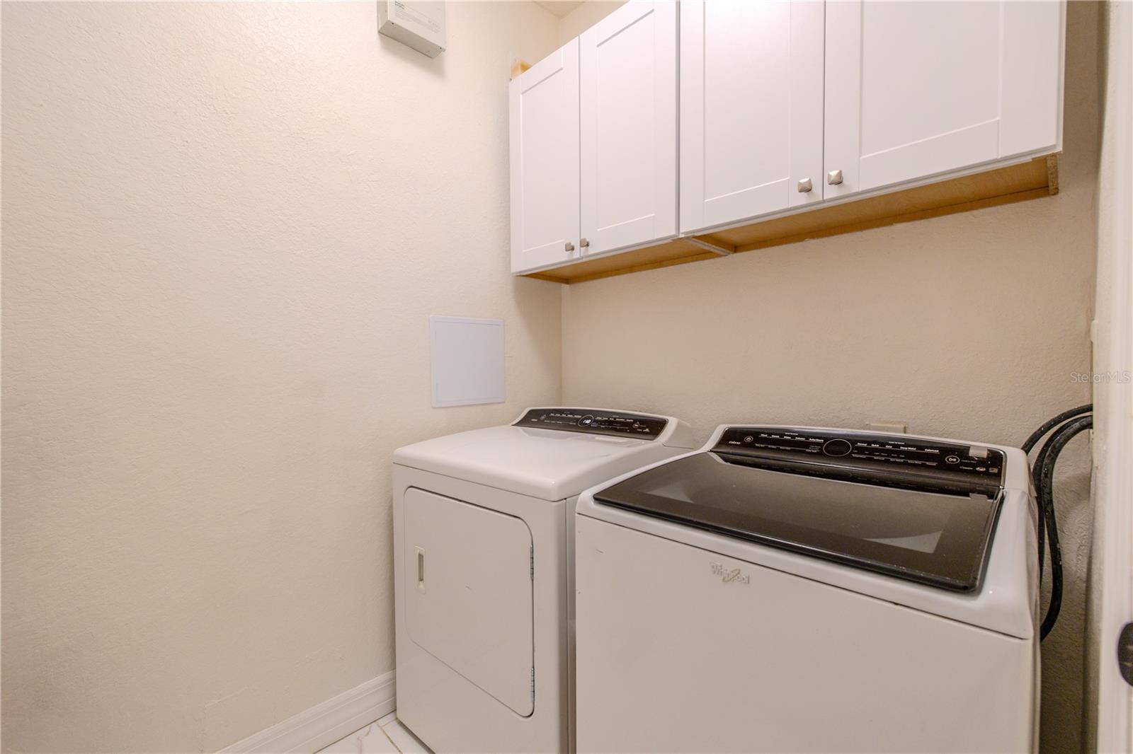 The laundry room is neatly tucked away and thoughtfully designed, featuring a full-size washer and dryer with upper cabinetry for convenient storage. Neutral finishes keep the space bright and functional, while the efficient layout makes everyday laundry tasks easy and organized without taking up valuable living space.