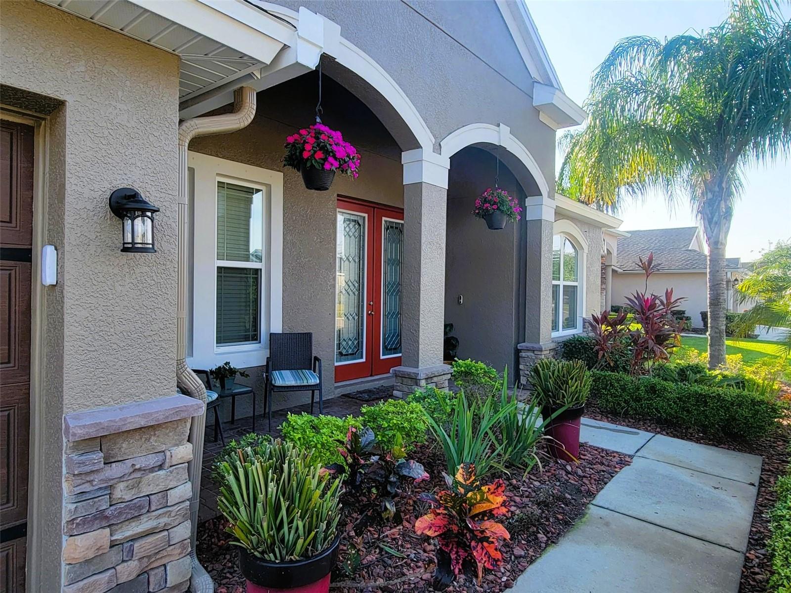 Mature landscaping, palm trees, and a covered entry create a welcoming first impression with elegant double doors