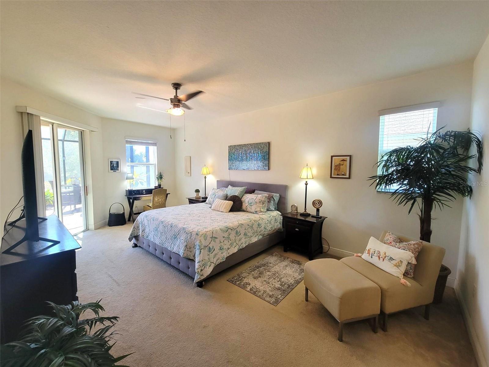 Spacious primary bedroom featuring plush carpeting, ceiling fan, and sliding glass doors leading directly to the covered lanai.