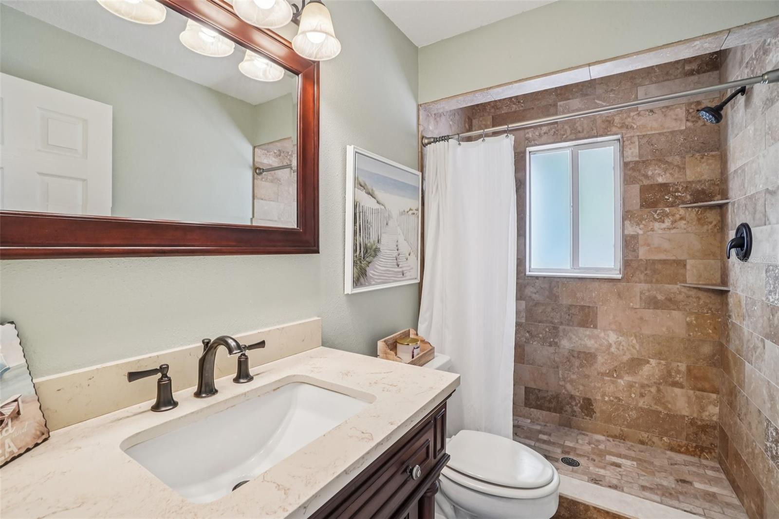 Bathroom 1 – Shower & Vanity ViewThe walk-in shower is finished with full tile surround, built-in niche shelving, and a window for natural light, paired with a clean, updated vanity for a refreshed look.