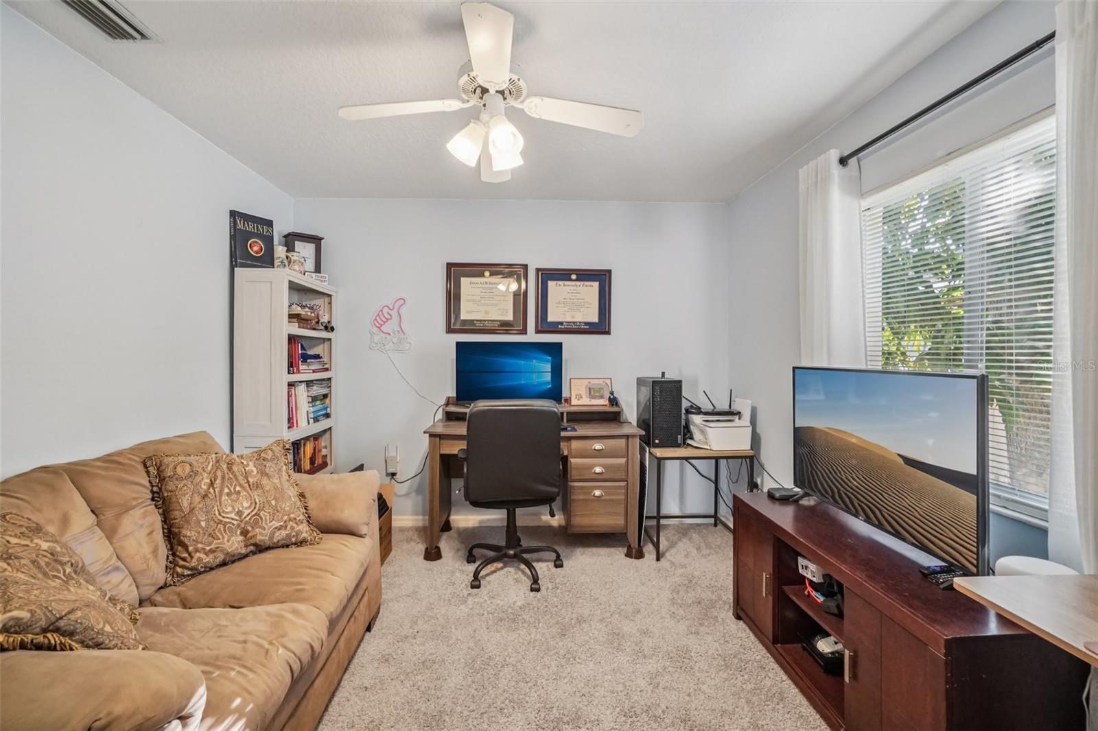 Bedroom 2 – This comfortable bedroom features soft carpeting, neutral wall tones, and a ceiling fan with light kit, offering a versatile space suitable for a bedroom or home office setup.