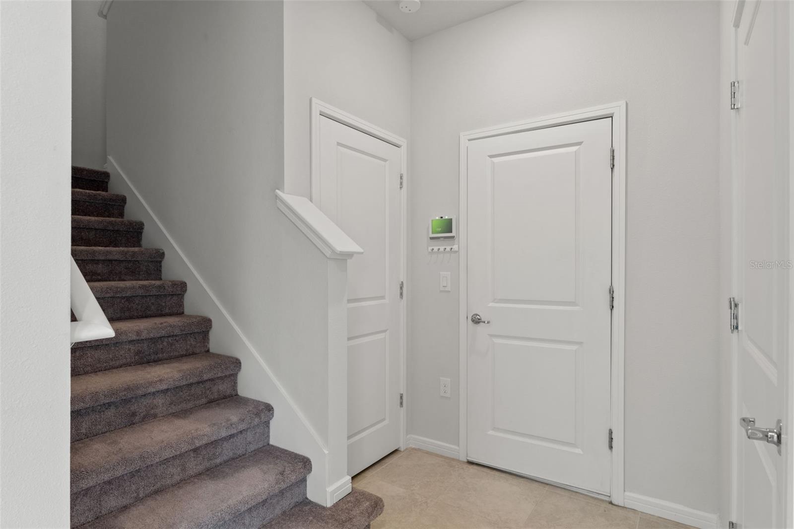 Bright entryway with tile flooring, neutral finishes, and a carpeted staircase leading to the upper level