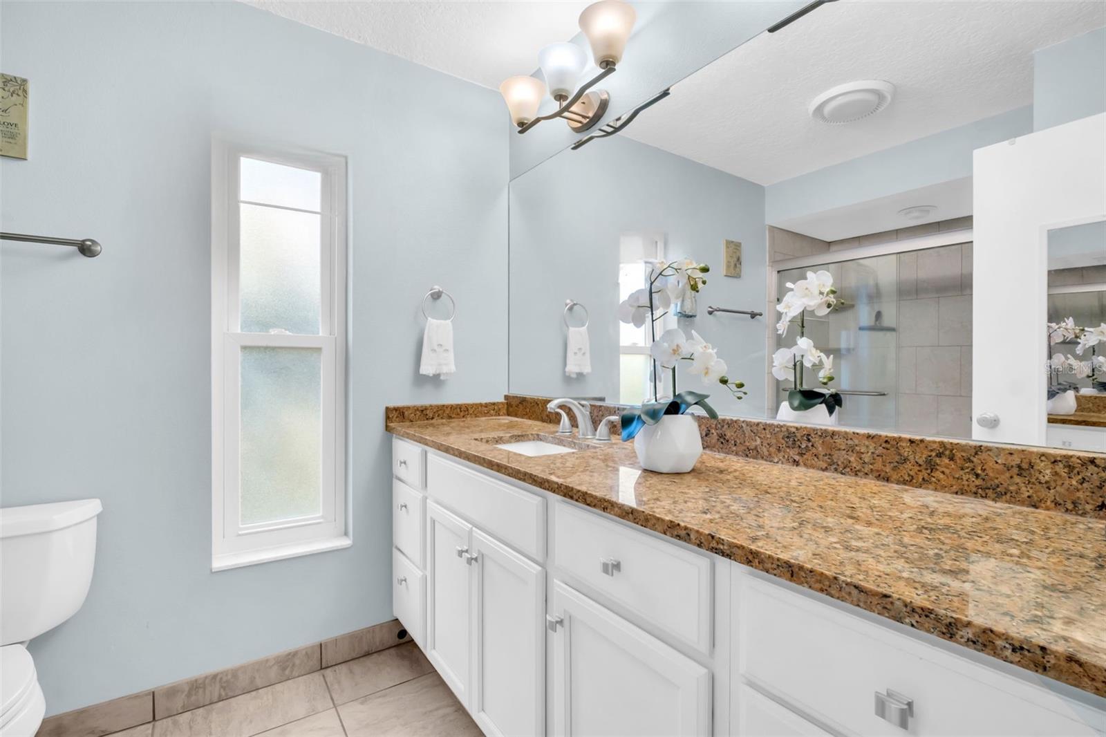 Updated primary en-suite with an oversized vanity, granite countertops, & updated lighting~
