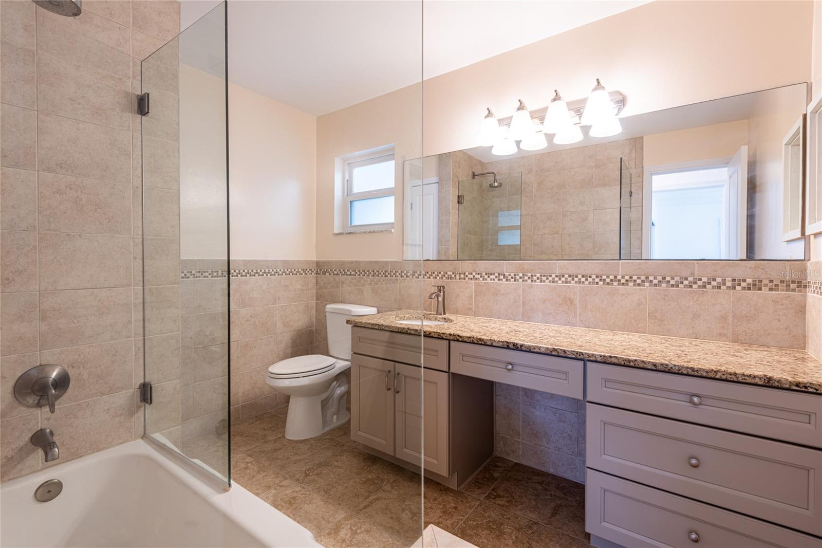 Bathroom 2 with wood cabinets, granite, and glass enclosed shower/tub combination