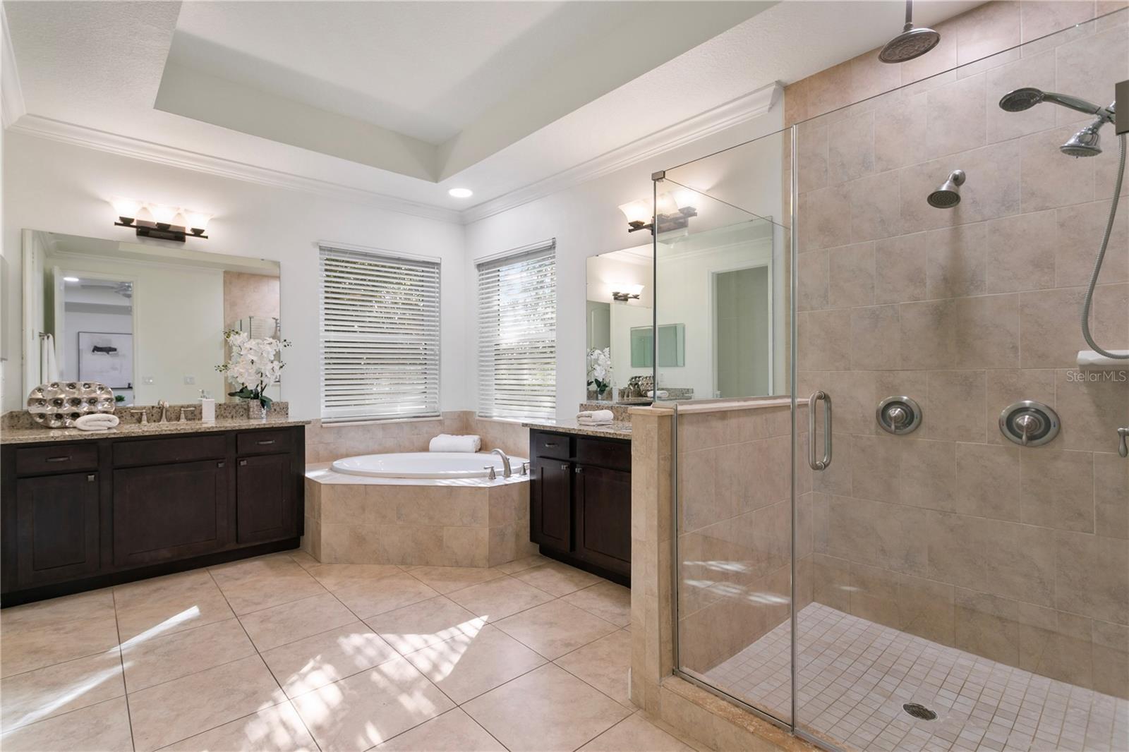 The spa-like en-suite bath features a garden tub, glass-enclosed shower with rainforest and multi-head fixtures, and dual granite-topped vanities.
