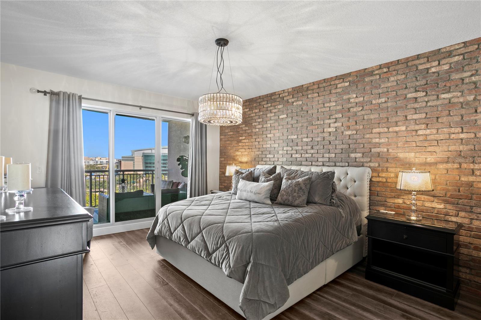 Spacious primary bedroom featuring brick wall detail and balcony access.