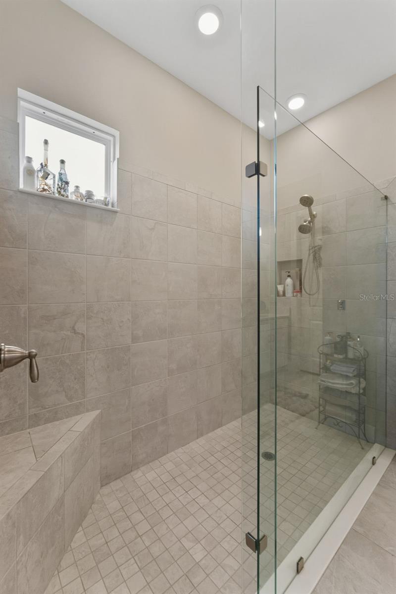 The primary bathroom features and oversized walk-in shower with a bench and frameless glass enclosure, and a high window to provide natural light.
