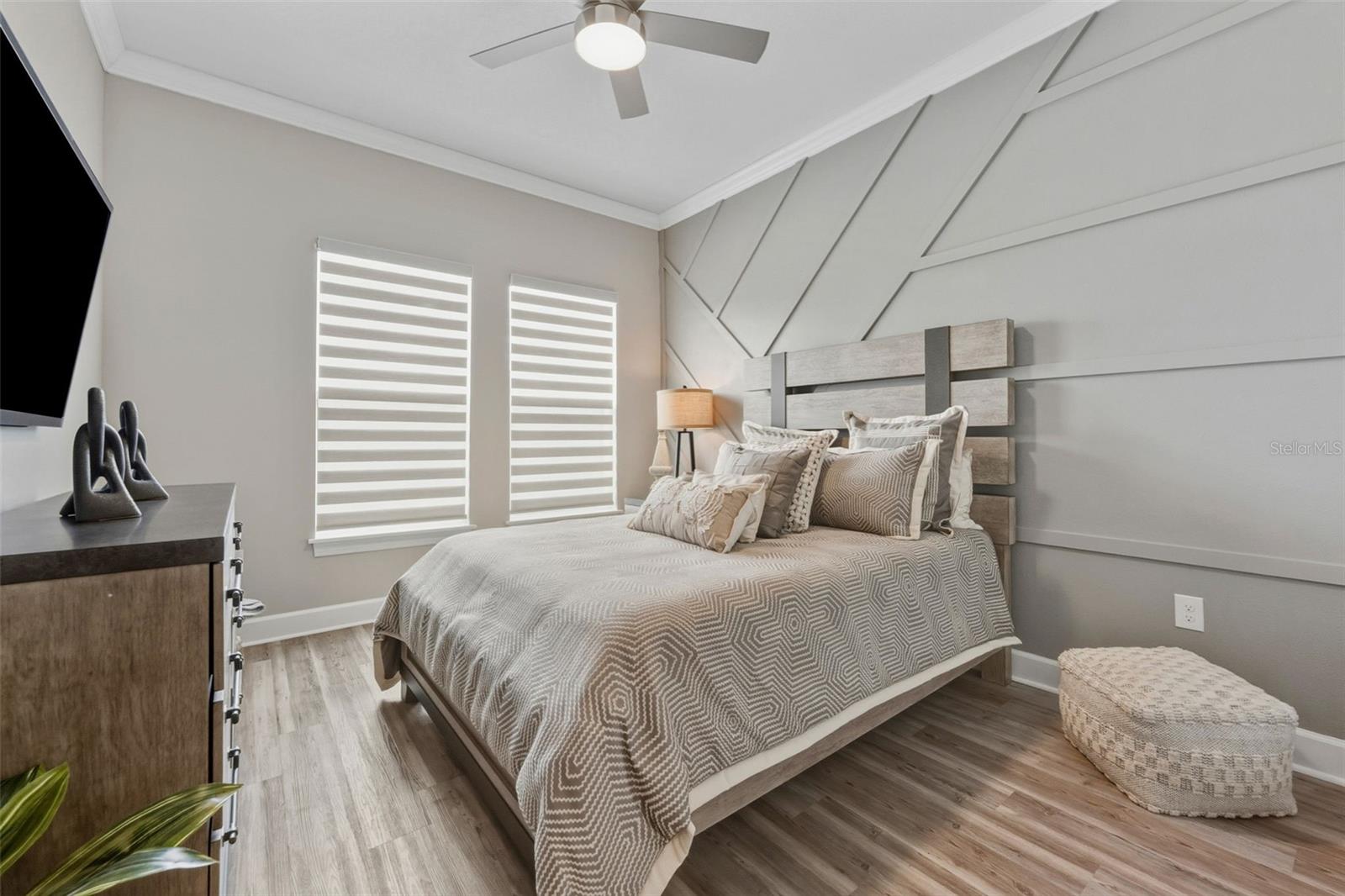 Bedroom 2 at the front of the home has crown molding and a custom wall. There are also zebra shades providing privacy with filtered light in the room.