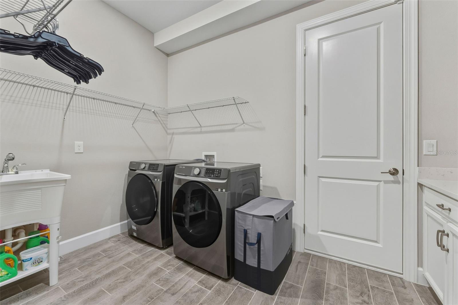 An over-sized indoor laundry room offers space and storage with a laundry sink, cabinets and countertop.