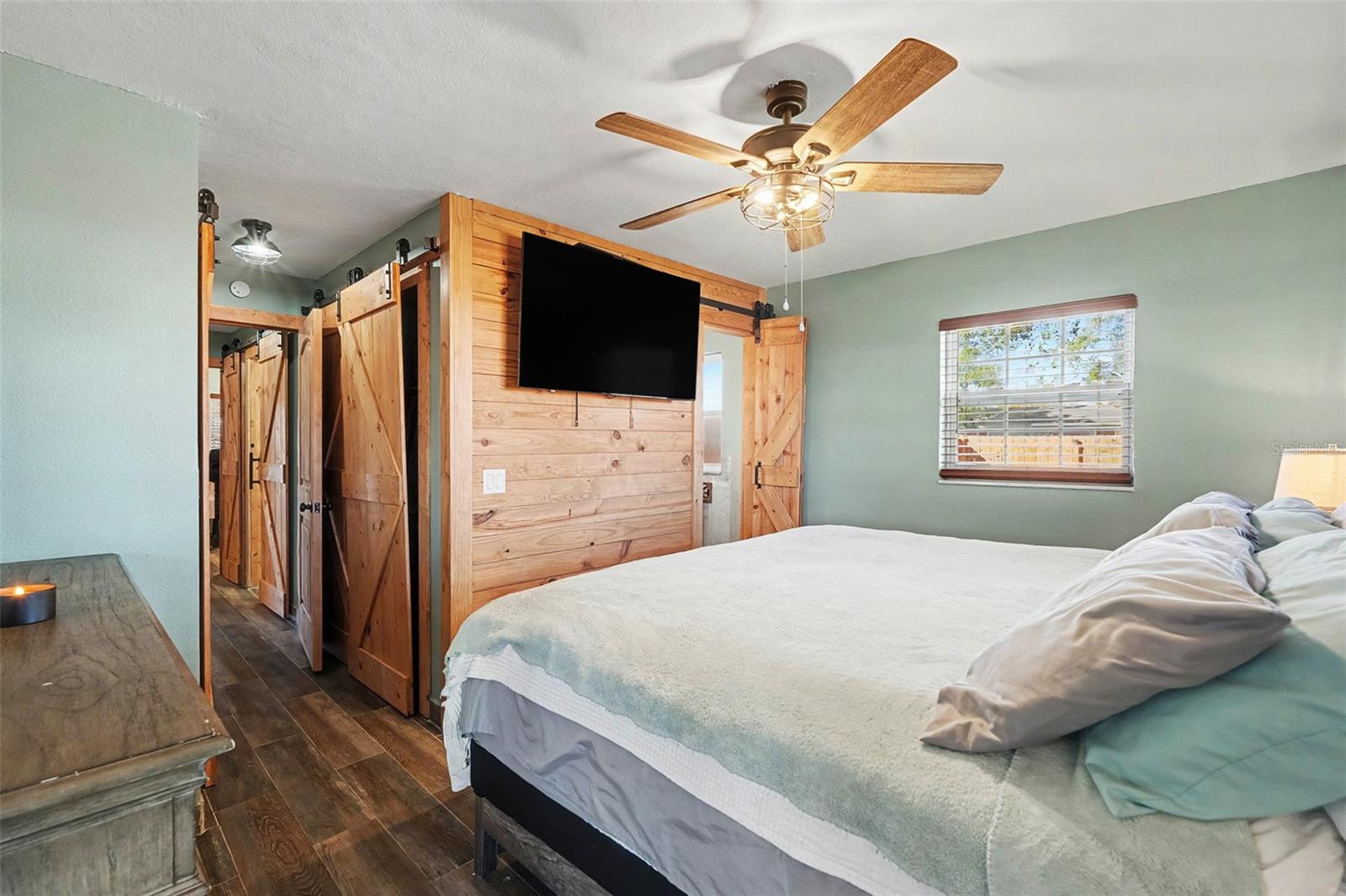 Spacious primary bedroom with wood-look tile flooring, custom barn doors, ceiling fan, and plenty of natural light.