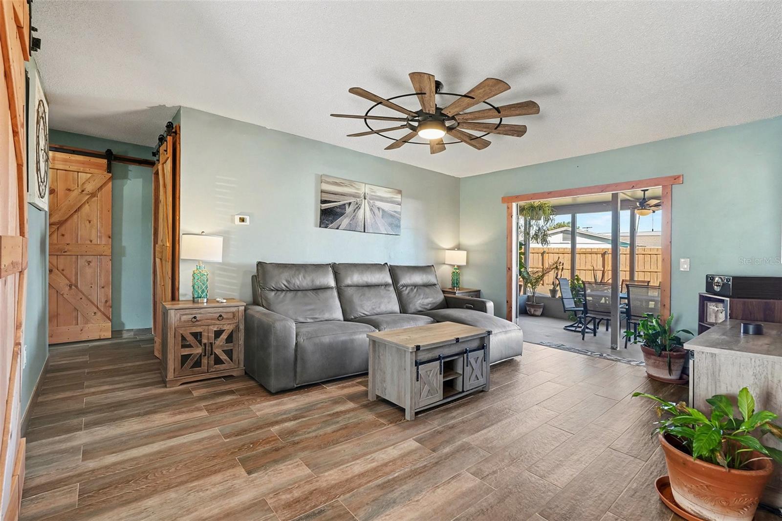 Bright and welcoming living room featuring wood-look tile flooring, stylish ceiling fan, and an open flow to the outdoor living space.