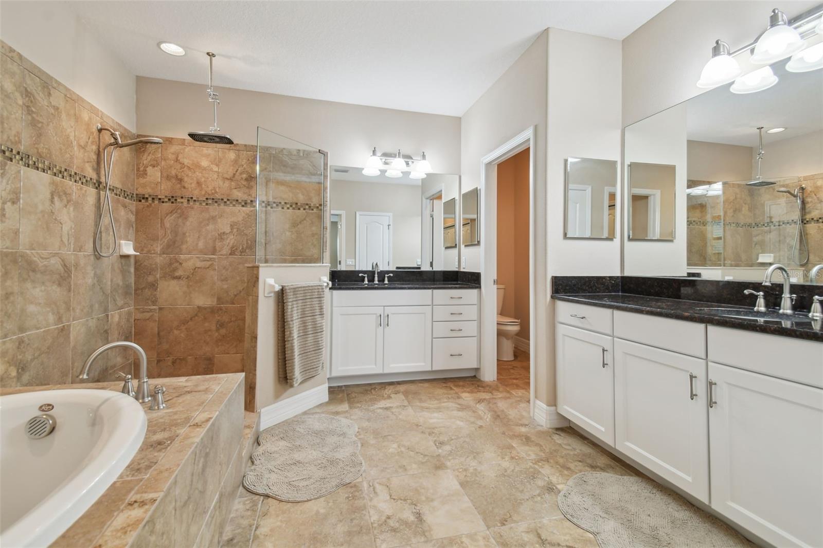 There is a large walk-in shower with a rain showerhead, wall spray showerhead, separate vanities, and a large soaking tub for relaxing after a long day!
