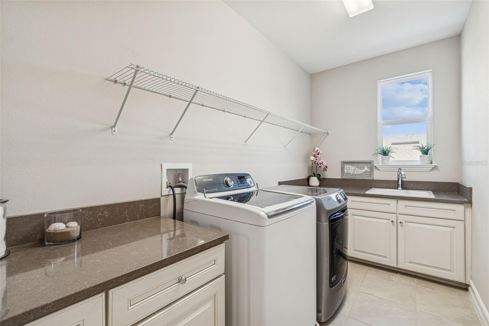 Upper-level laundry room with storage, counter space, utility sink, and natural light