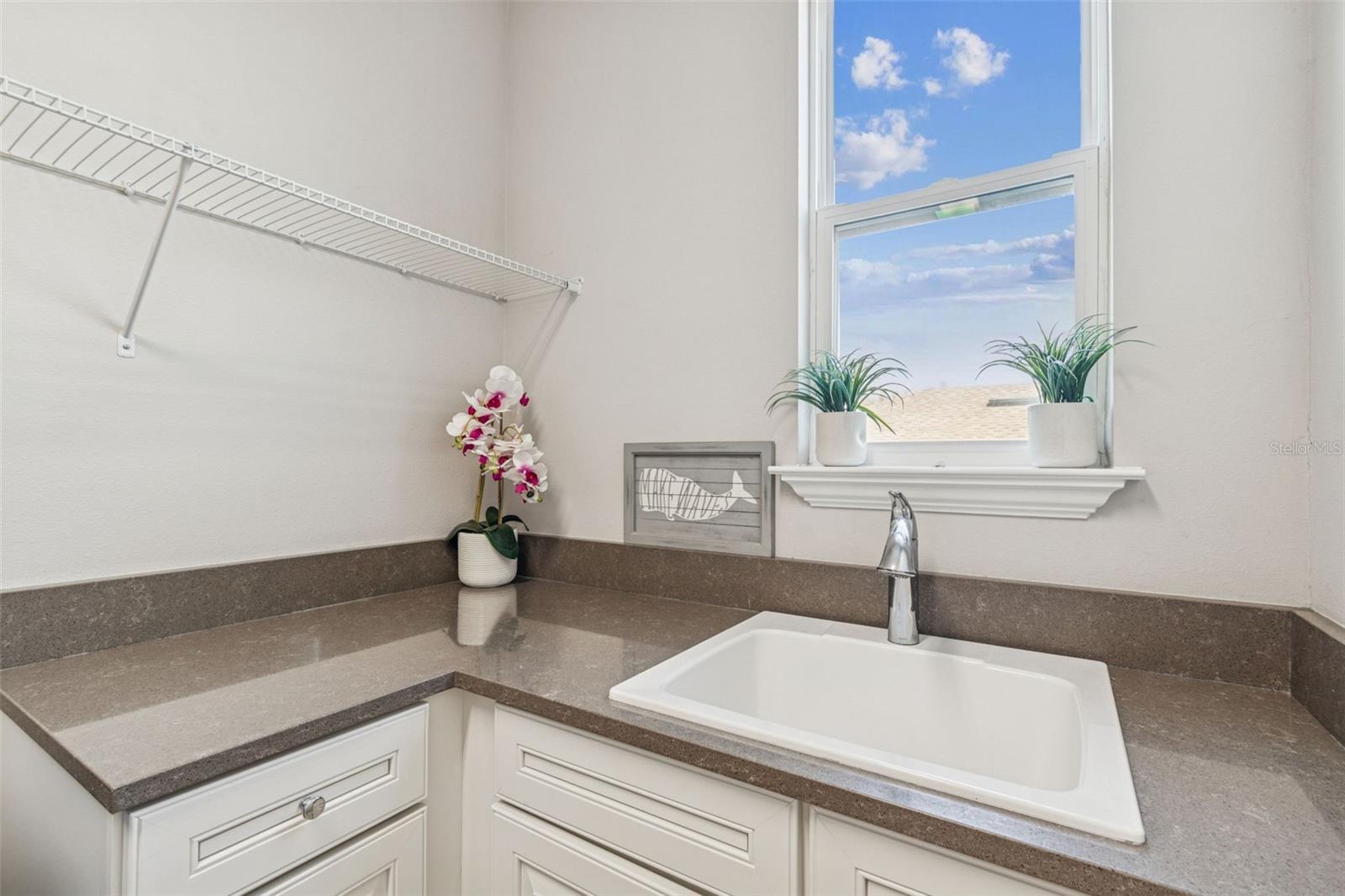 Upper-level laundry room with storage, counter space, utility sink, and natural light