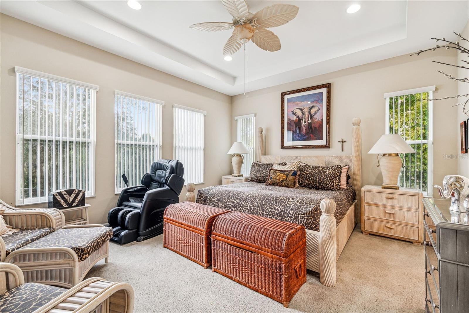 Primary suite showcasing tray ceiling, ceiling fan, and multiple windows overlooking conservation