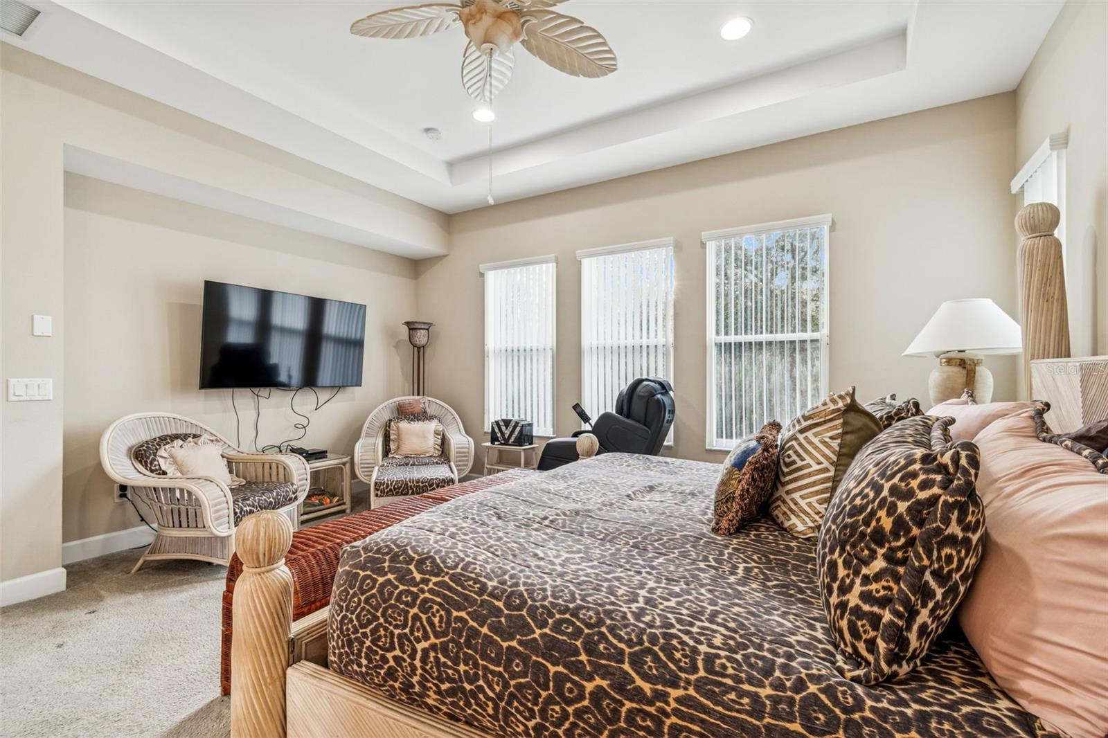 Primary suite showcasing tray ceiling, ceiling fan, and multiple windows overlooking conservation