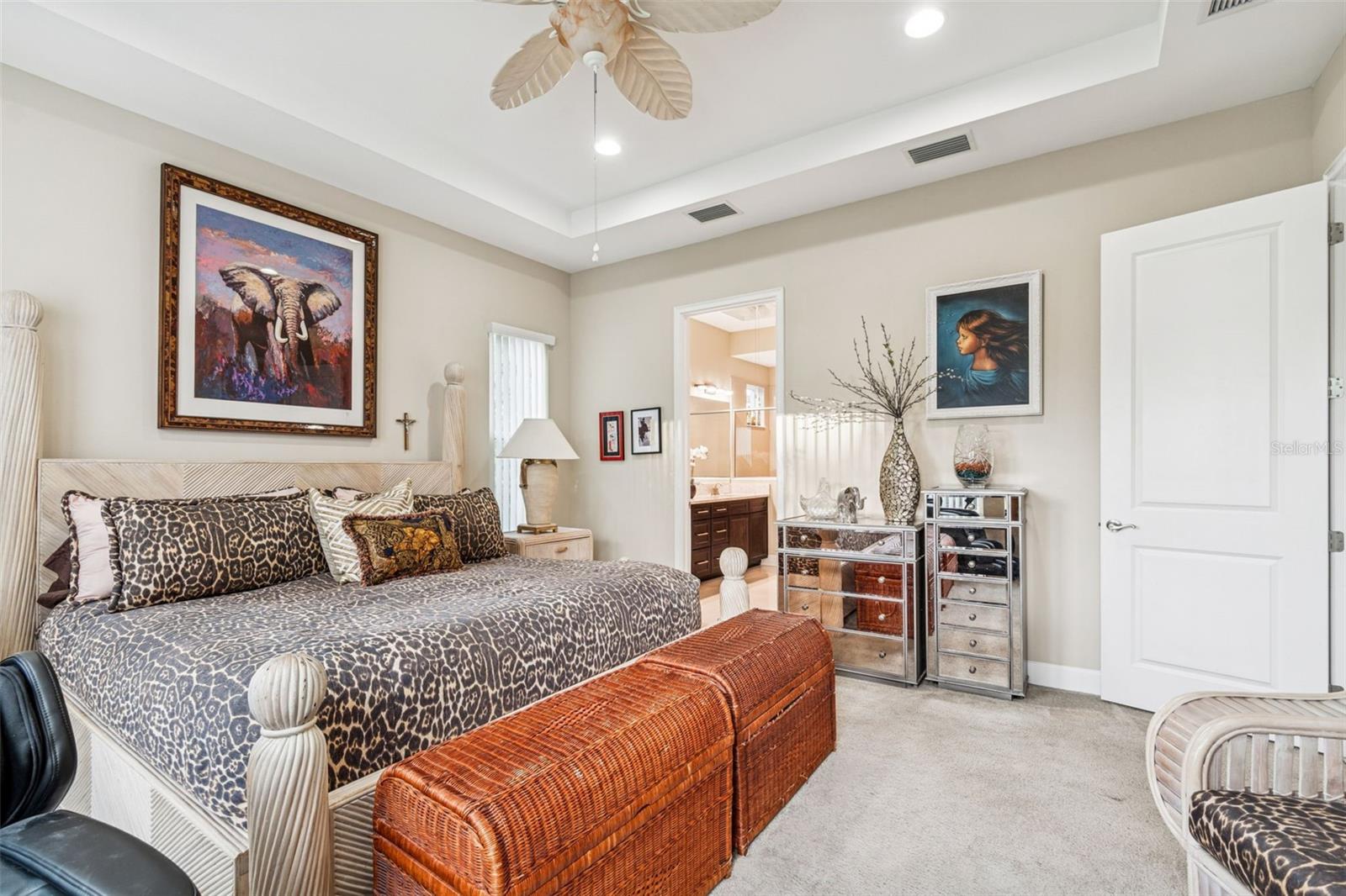 Primary suite showcasing tray ceiling, ceiling fan, and multiple windows overlooking conservation