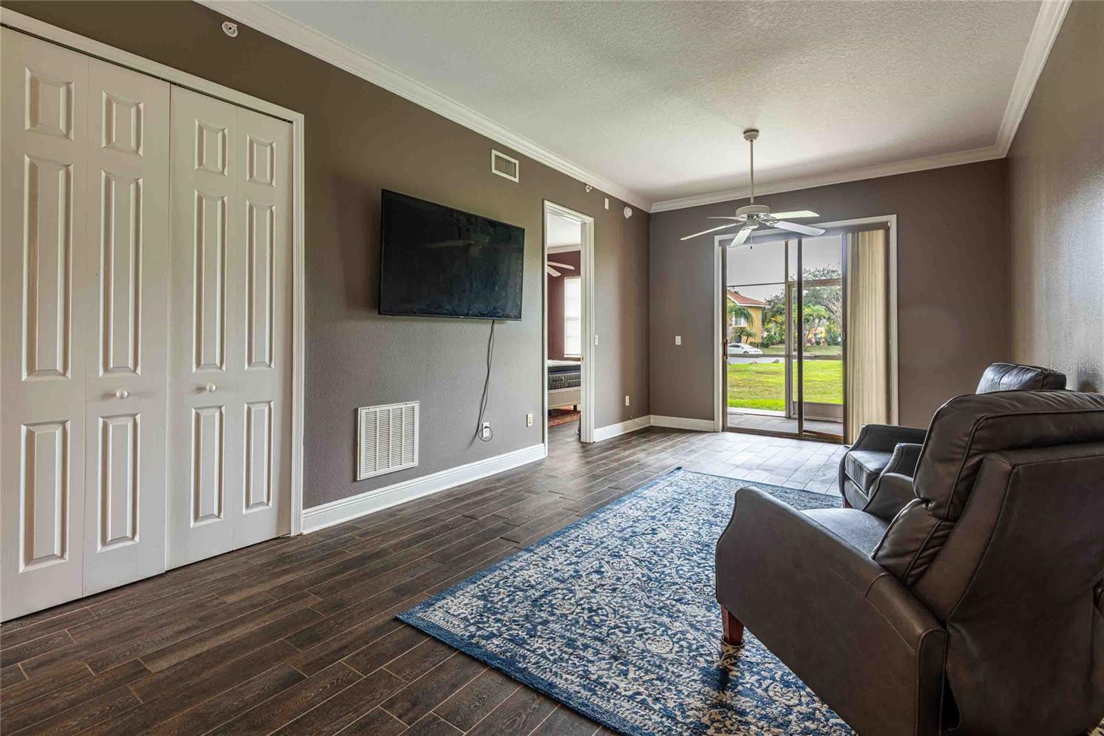 Living room with doors that open to work station. 2 matching chairs and large TV remain