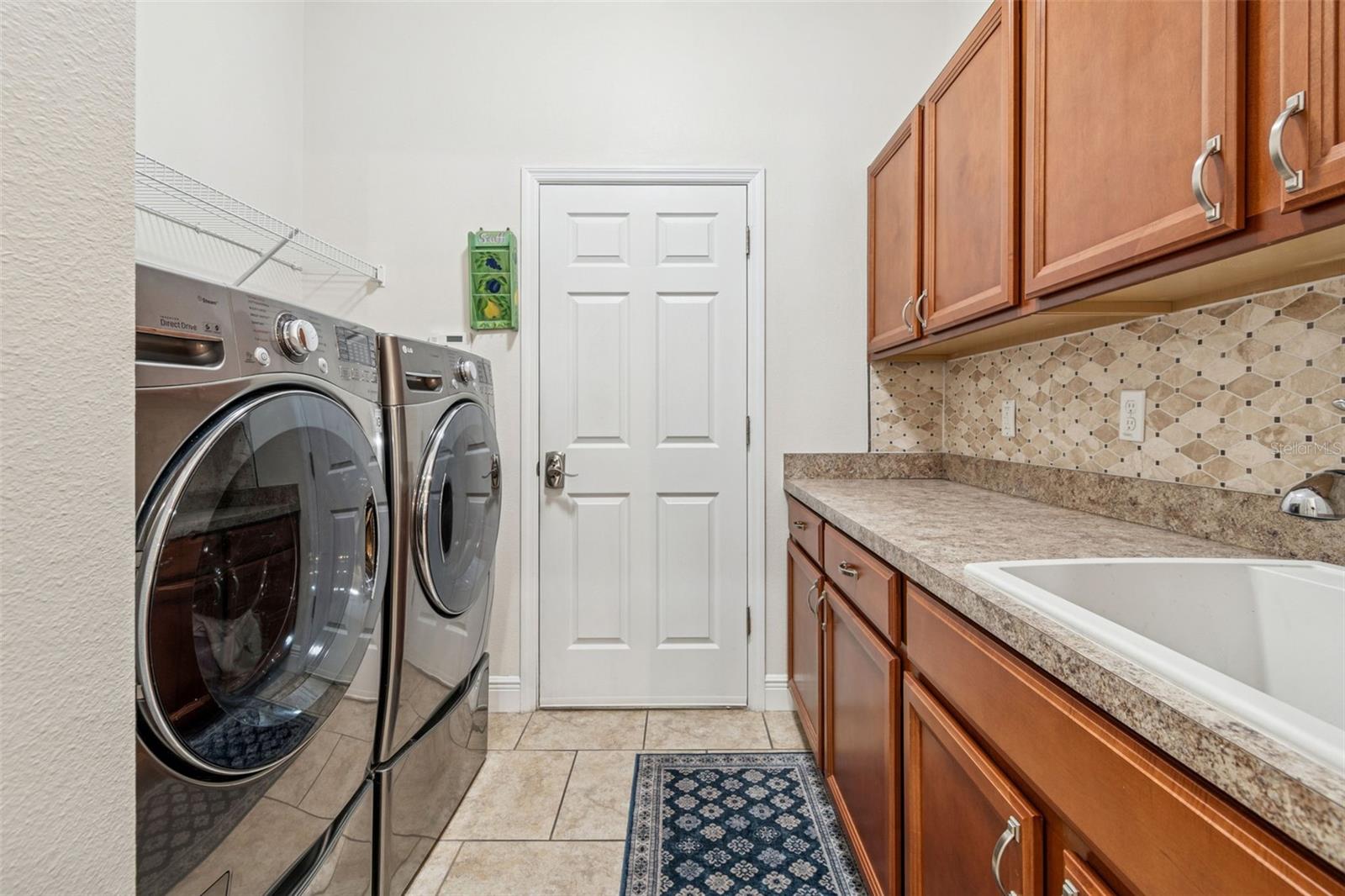 This photo features a well-appointed laundry room with ample cabinetry, counter space, and a utility sink, and the washer and dryer are included with the sale, adding convenience and value for the next owner.
