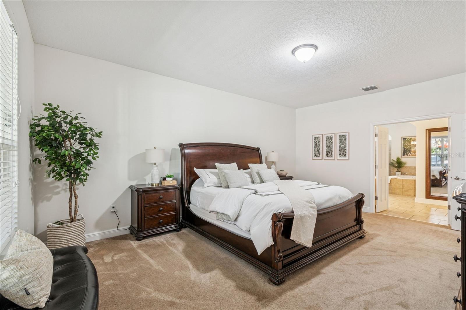 This photo showcases the spacious primary bedroom, where elegant French doors open directly to a large primary bath, creating a private retreat with a seamless flow between the sleeping and spa-like bathing areas.