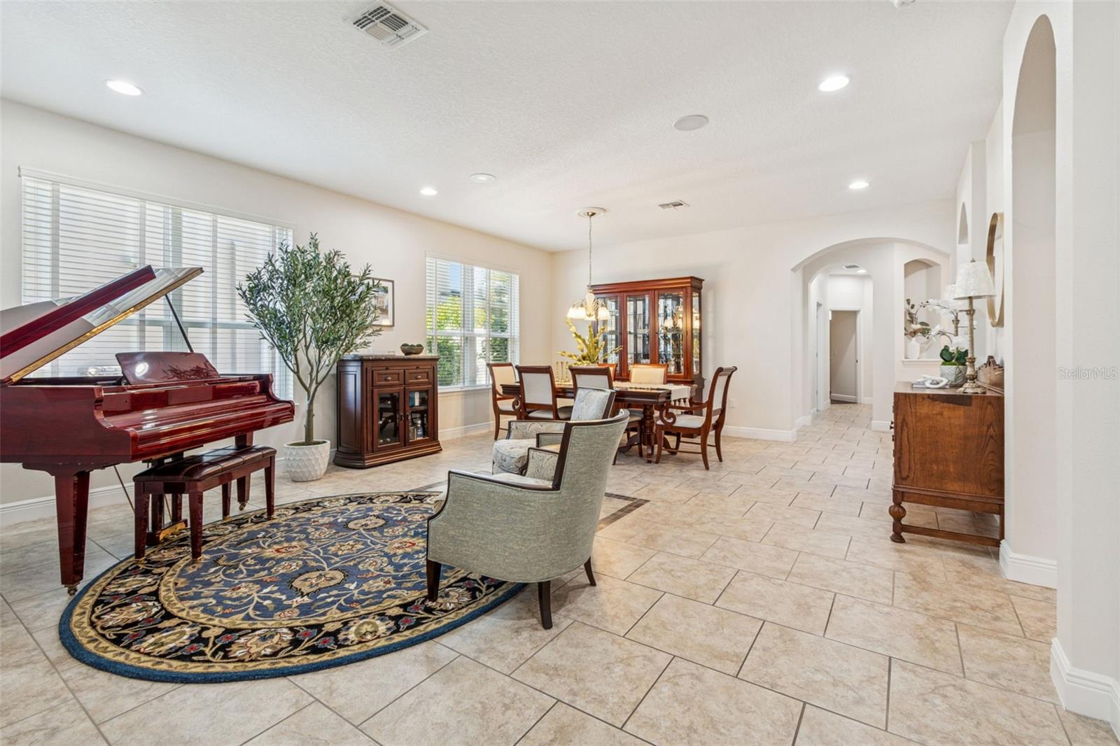 A bright, open living and dining area with tile floors, large windows, recessed lighting, and arched doorways  create a warm, refined atmosphere