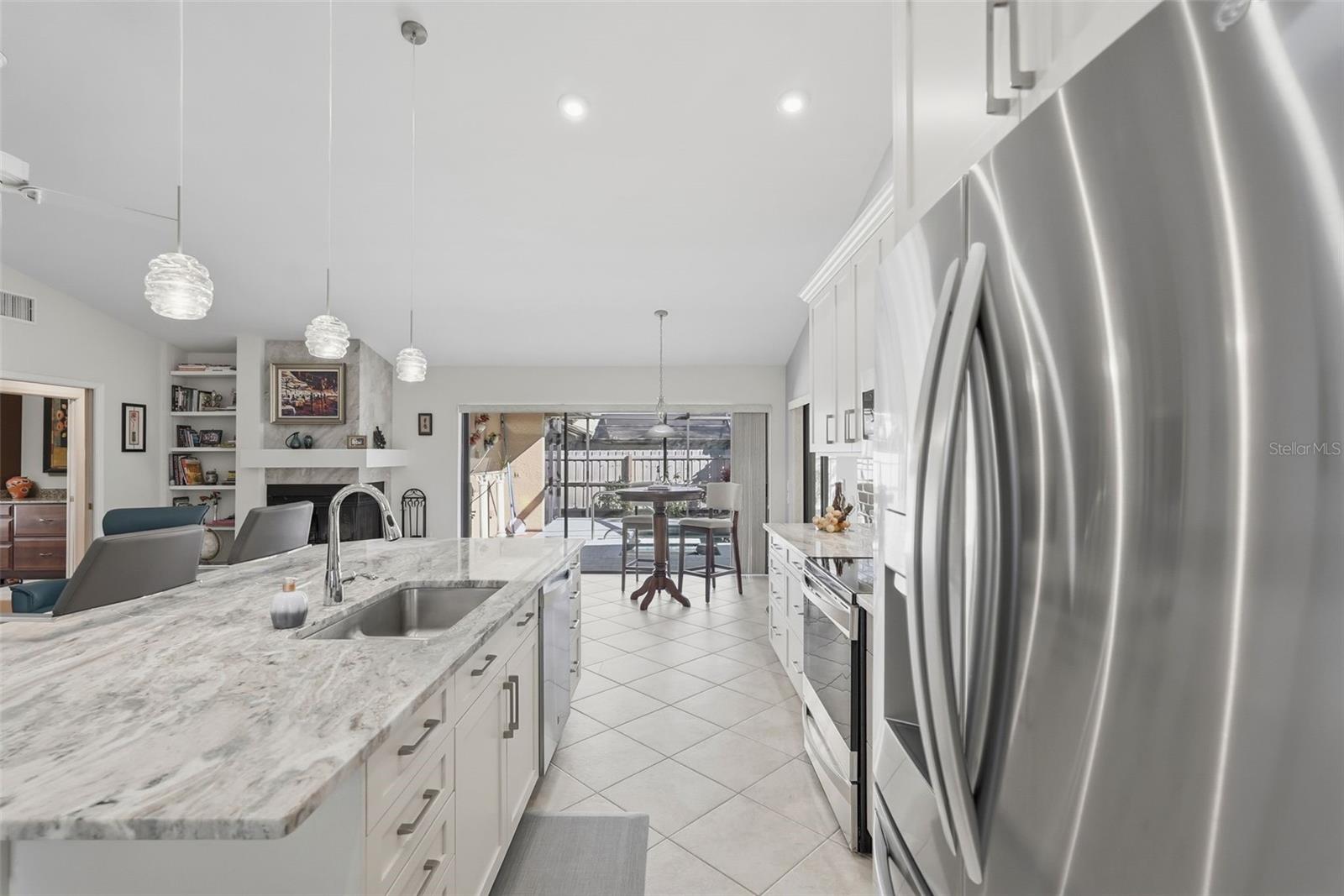Different view of the kitchen and attached leisure room with wood burning fire place, built in shelves and sliding doors open to the screened in pool.