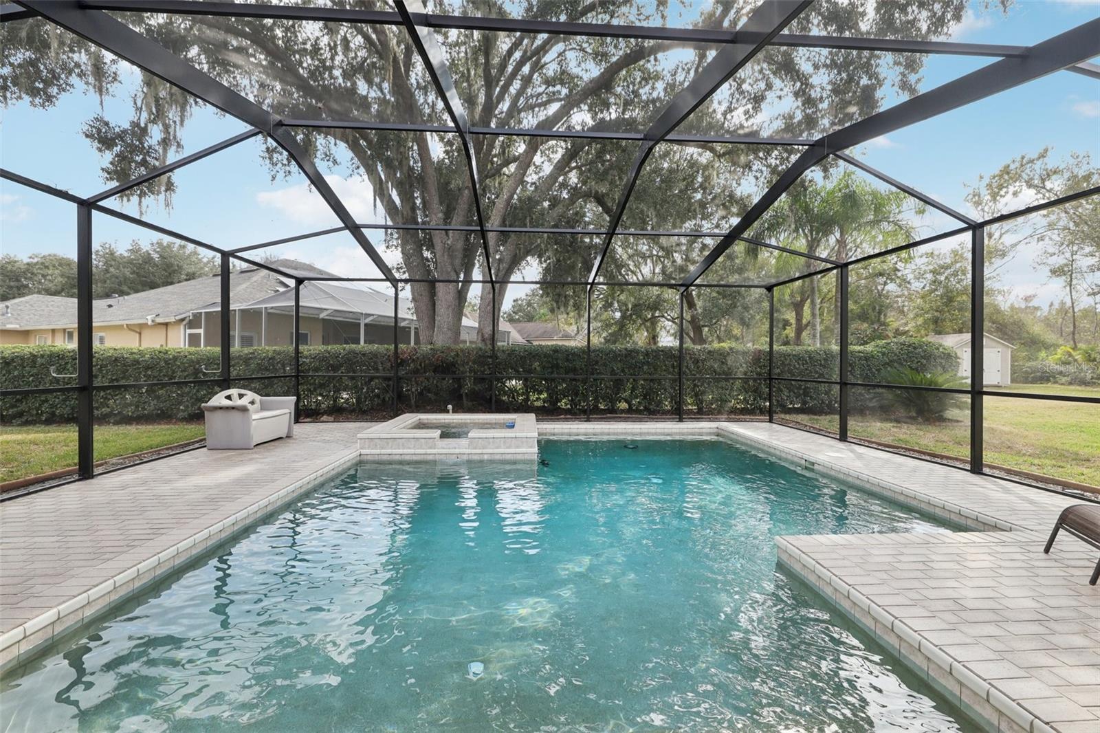 Screened pebble tech pool adorned by beautiful pavers, heated spa and pool