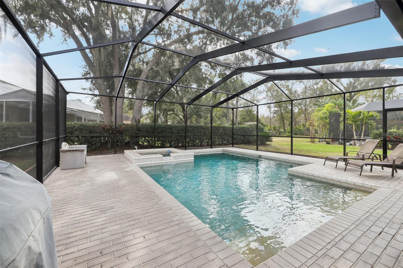 Screened pebble tech pool adorned by beautiful pavers, heated spa and pool