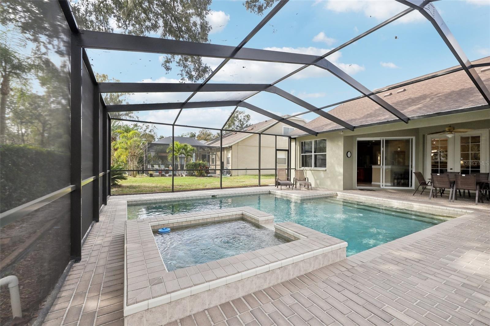 Screened pebble tech pool adorned by beautiful pavers, heated spa and pool