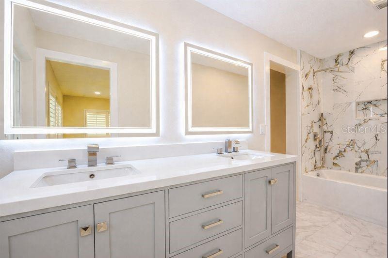 This Jack-and-Jill bath offers double LED-lighted mirrors, double sinks with a quartz countertop, marble floors, and beautifully tiled shower walls complete with a built-in niche & rain shower head.
