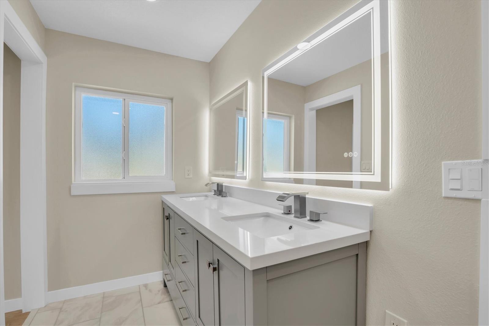 Double sinks, abundant natural light, & elegant tilework elevate this bathroom’s spacious, luxurious feel.