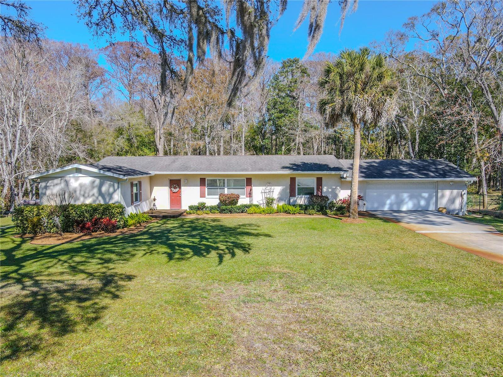 Single-story 3/2/2 ranch-style home set on 1.7 acres, framed by mature trees and a wide, open front lawn.