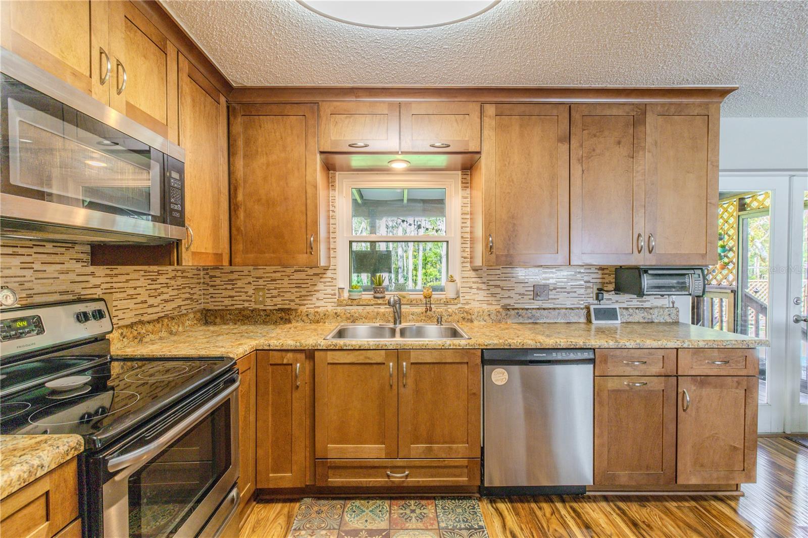 Functional kitchen workspace with granite countertops, tile backsplash, double-basin sink beneath a window, and under-cabinet lighting, offering both task efficiency and natural light.