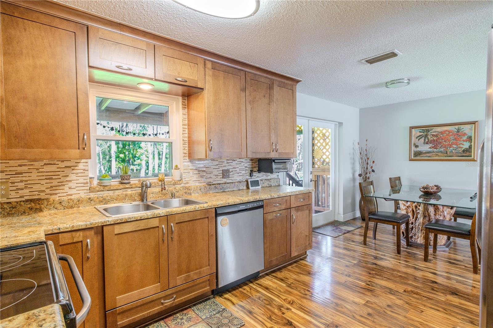 Kitchen opens to the dining area, featuring laminate flooring throughout, granite counters, and sliding glass doors that provide access to the rear deck and wooded views beyond.