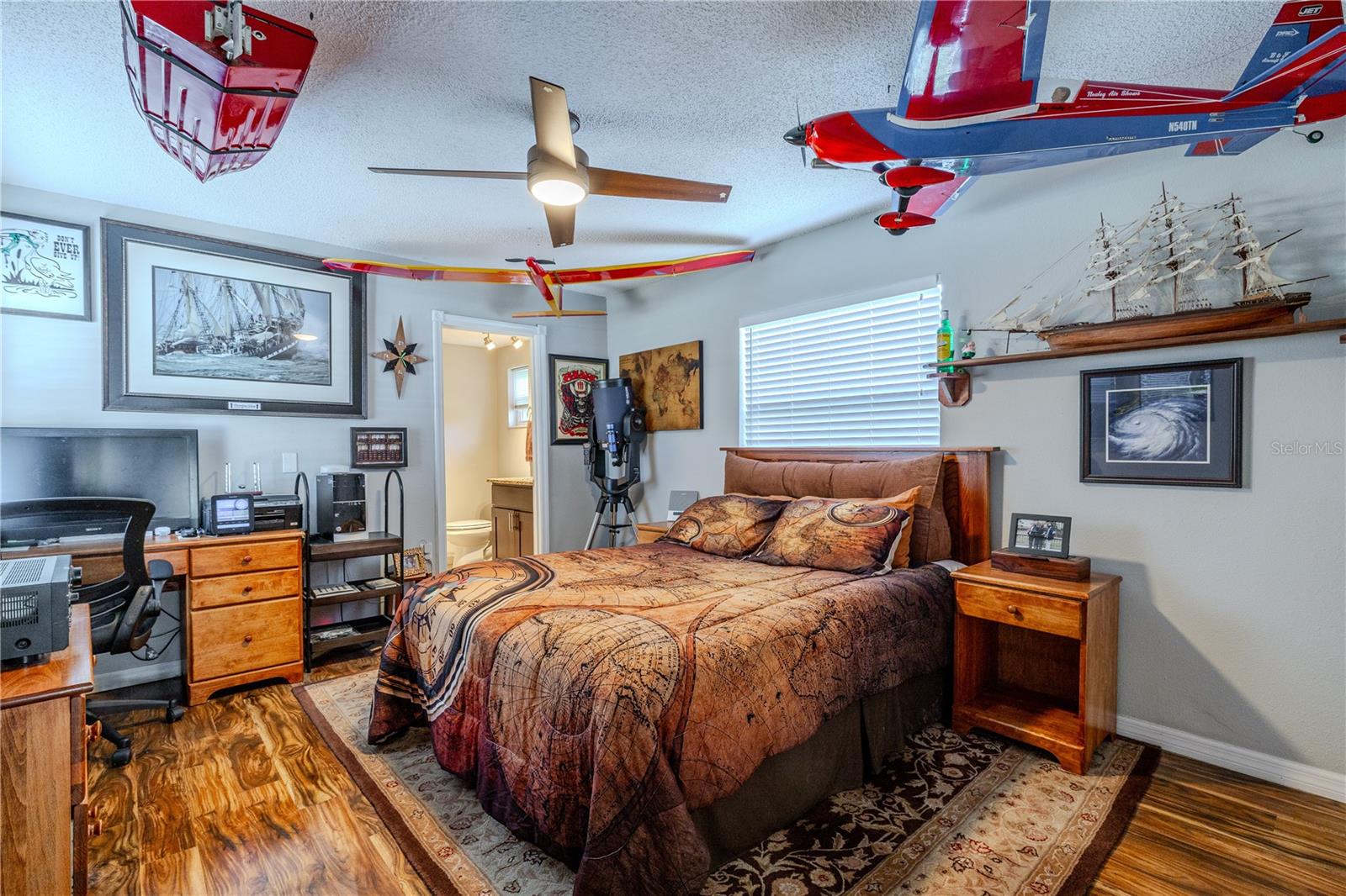 Spacious primary bedroom featuring wood-look laminate flooring, soft neutral wall tones, and a centered ceiling fan with integrated light for year-round comfort. The well-proportioned layout easily accommodates a full bedroom suite while maintaining clear pathways and visual balance.