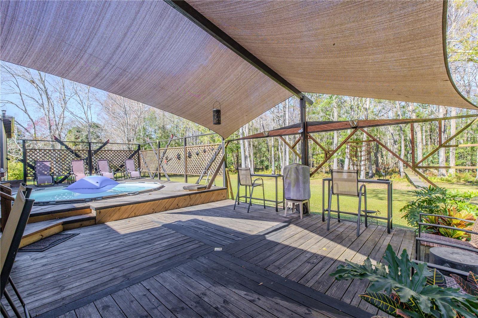 Spacious wood deck with multi-directional plank design and built-in shade structure, connecting seamlessly to the pool area and yard.