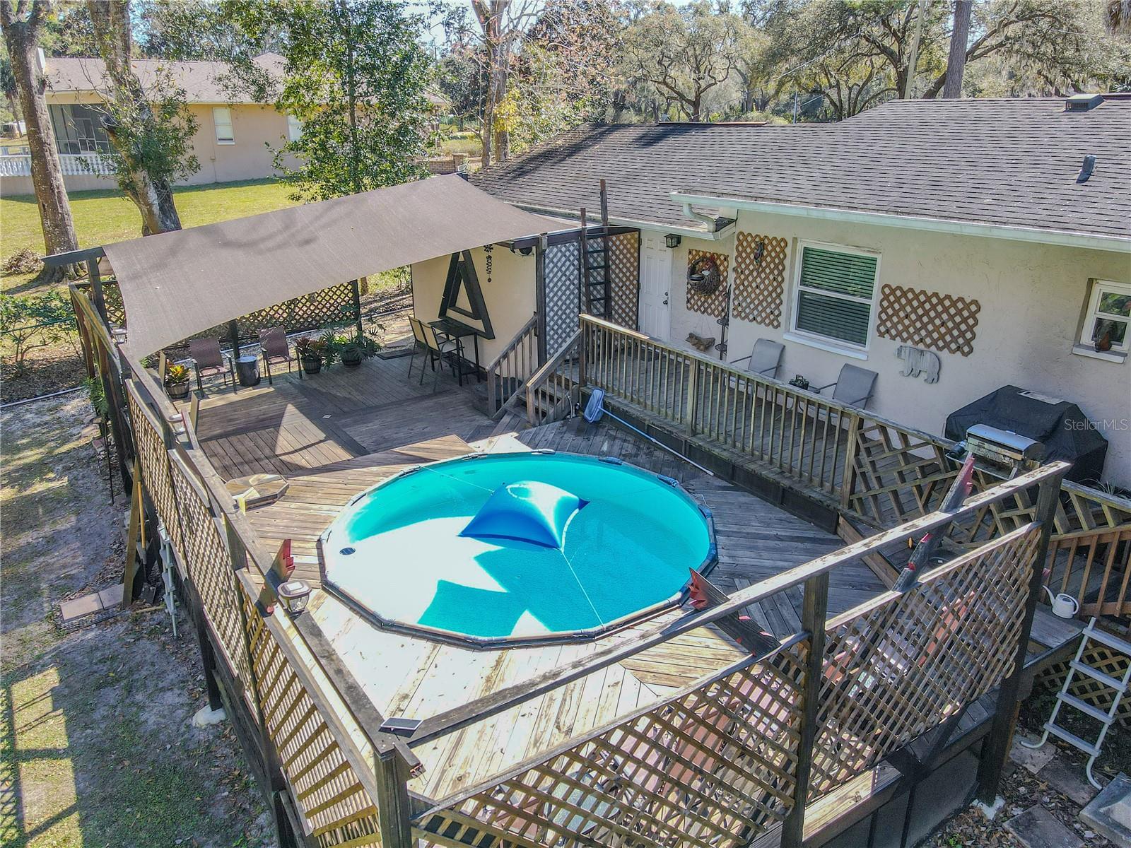 An elevated view highlights the full scope of the outdoor living space, including the above-ground pool, expansive decking, and privacy latticework. The layout is thoughtfully designed to maximize space, privacy, and connection to the surrounding greenery.