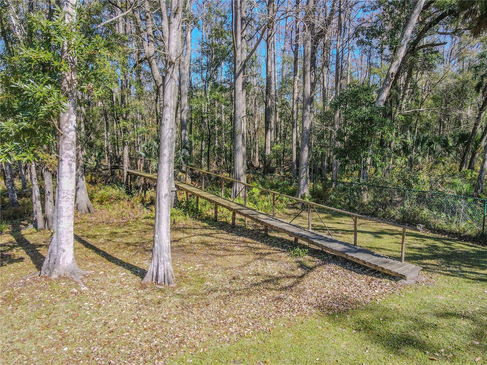 An 80-foot private wooden walkway leads into the wooded area, offering a quiet path through native trees and undergrowth toward Bear Creek just beyond the property line.