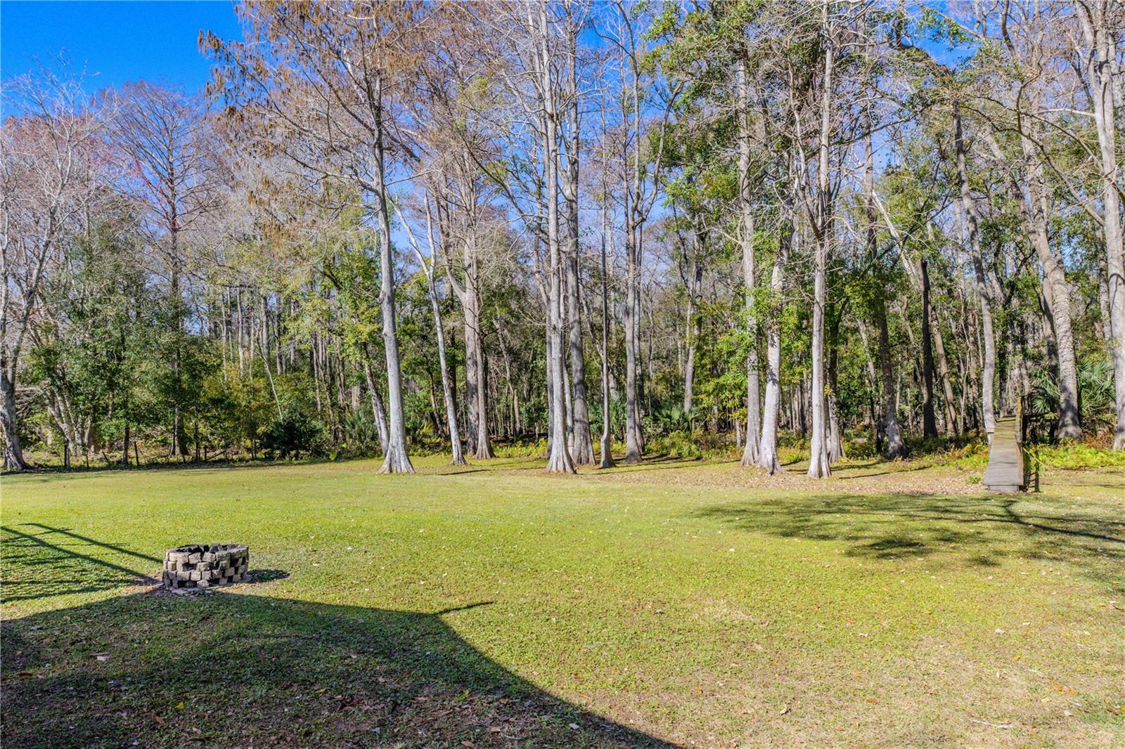 Wide open grassy yard with a dedicated fire pit area and direct access to the wooded surroundings
