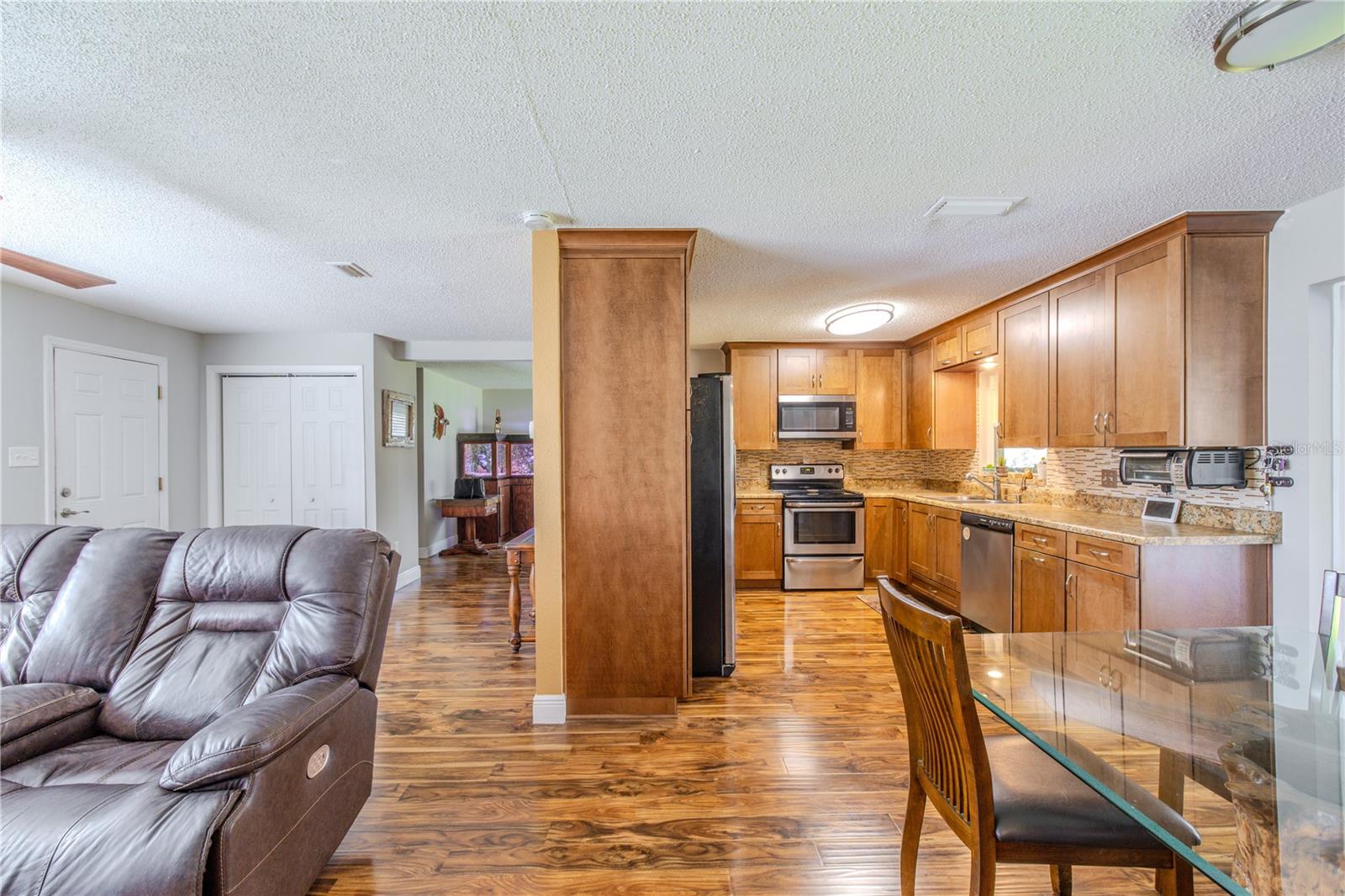 Open-concept view showcasing the living room, dining area, and kitchen, with laminate flooring throughout, warm wood cabinetry, and a functional layout designed that adapts easily to quiet nights or company.