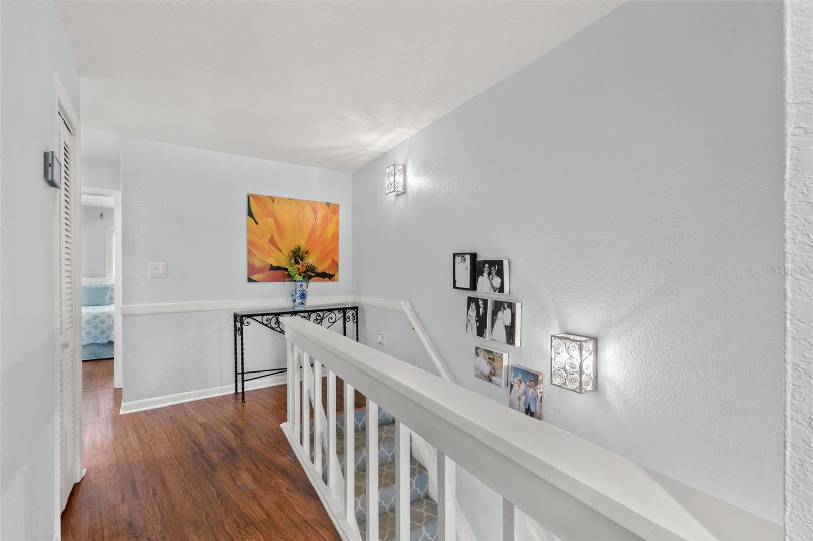 Upper-level hallway featuring wood flooring, recessed and wall-mounted lighting, and an open railing that overlooks the staircase, creating a bright and connected transition between rooms.