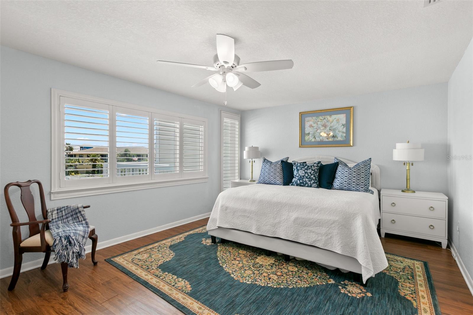 Spacious primary bedroom featuring wood flooring, soft neutral walls, plantation shutters, and a ceiling fan, creating a bright and comfortable retreat.