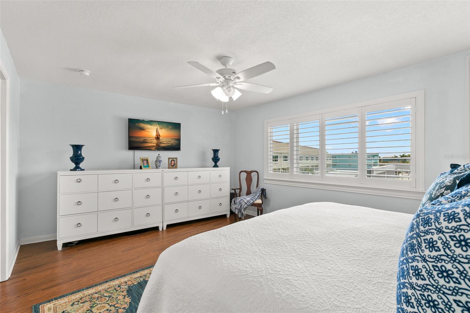 Alternate view of the primary bedroom highlighting generous wall space, large windows with shutters, and a well-balanced layout suitable for multiple furniture configurations.